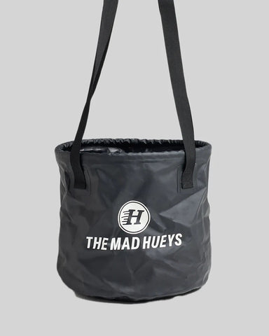 Hueys Dry Bucket Bag in black with waterproof 600D polyester design, twin carry straps, and plastisol Hueys logo print — perfect for beach, boat, and outdoor adventures.